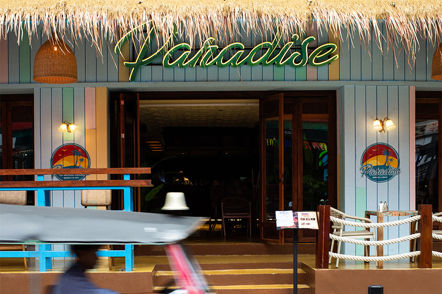 Daytime entrance of Paradise Soi 11 with its thatched roof and neon script sign